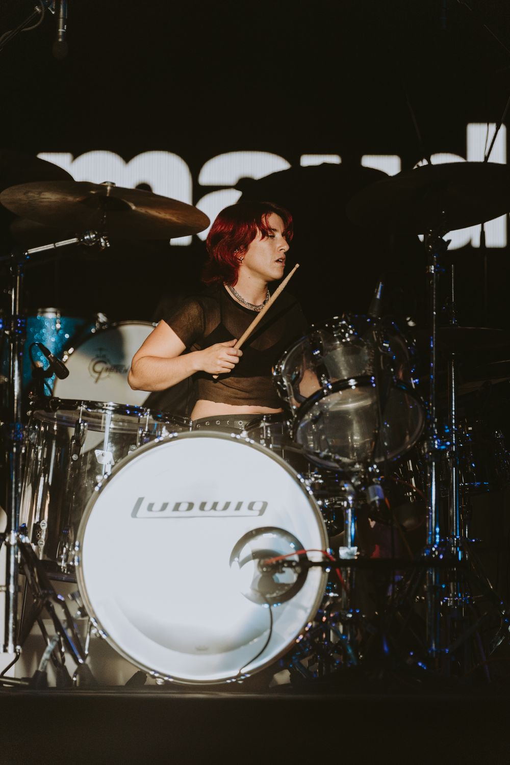 Drummer performing behind a Ludwig drum kit on dark stage with dramatic lighting.