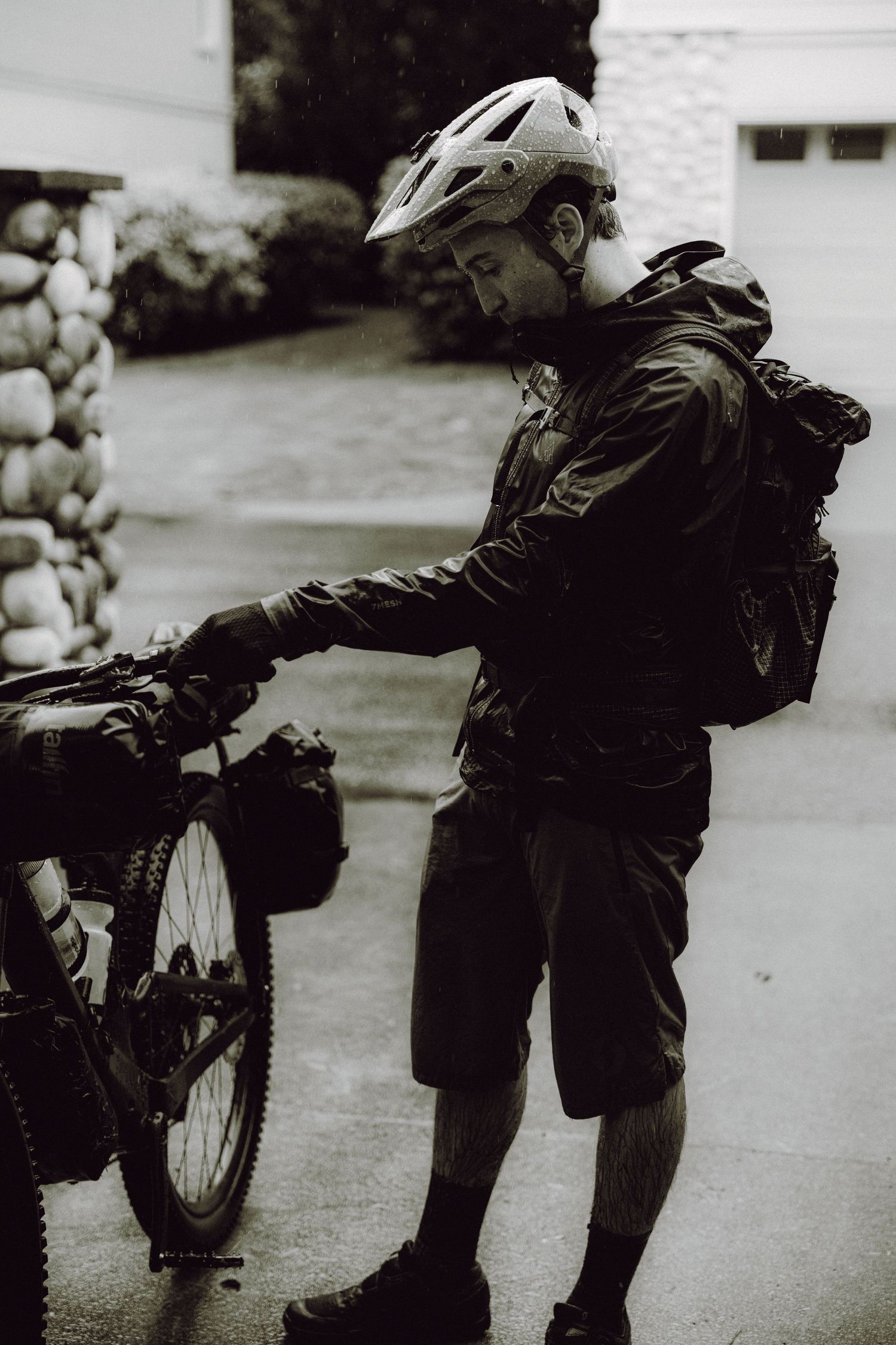 Cyclist in protective gear adjusting equipment on a mountain bike in black and white.