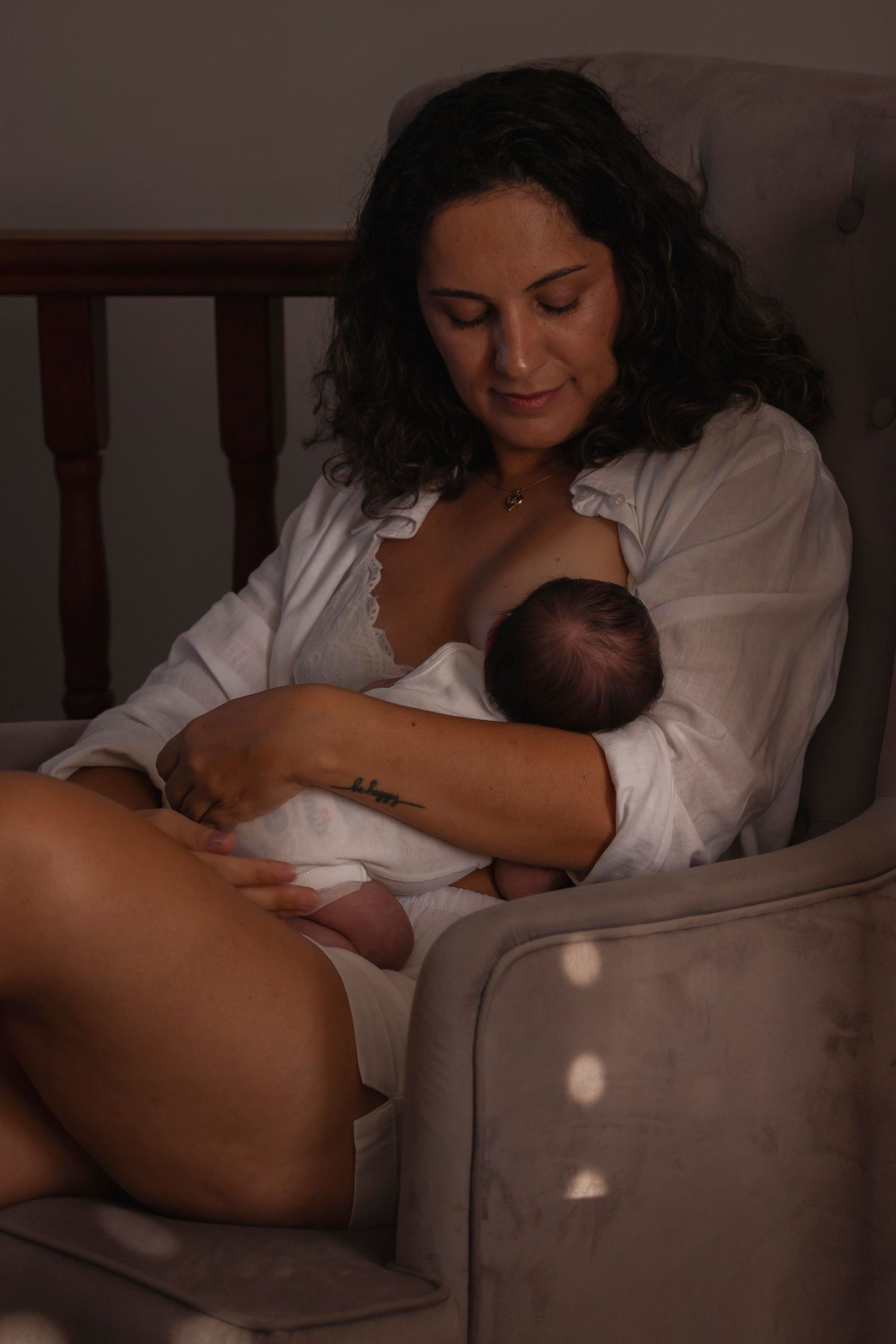 Newborn photography session. Intimate low-light photograph capturing a nurturing moment in a cozy setting.