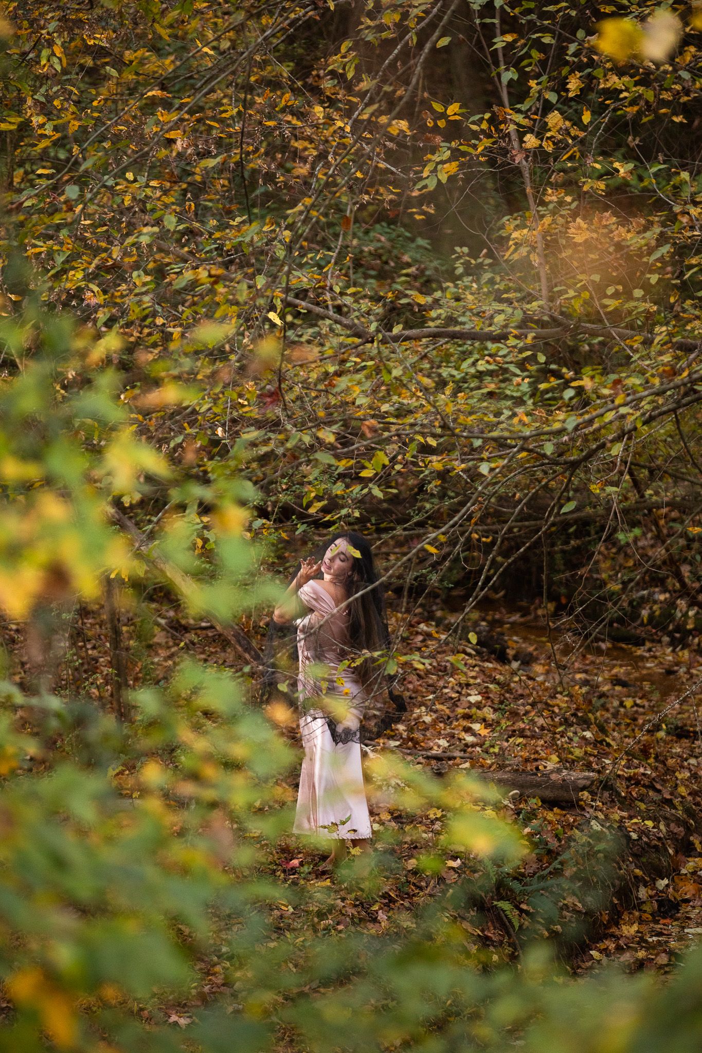 A small figure in a white dress explores an autumn forest setting with golden leaves scattered on the ground.