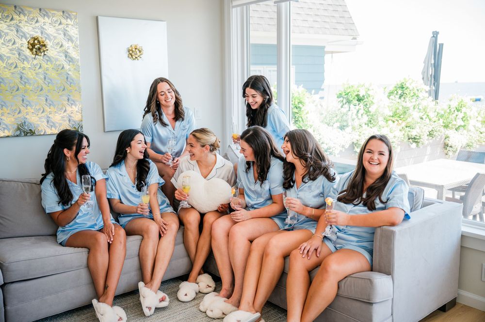 A group of friends in matching denim outfits laugh together while sitting on a gray couch in a bright living room.
