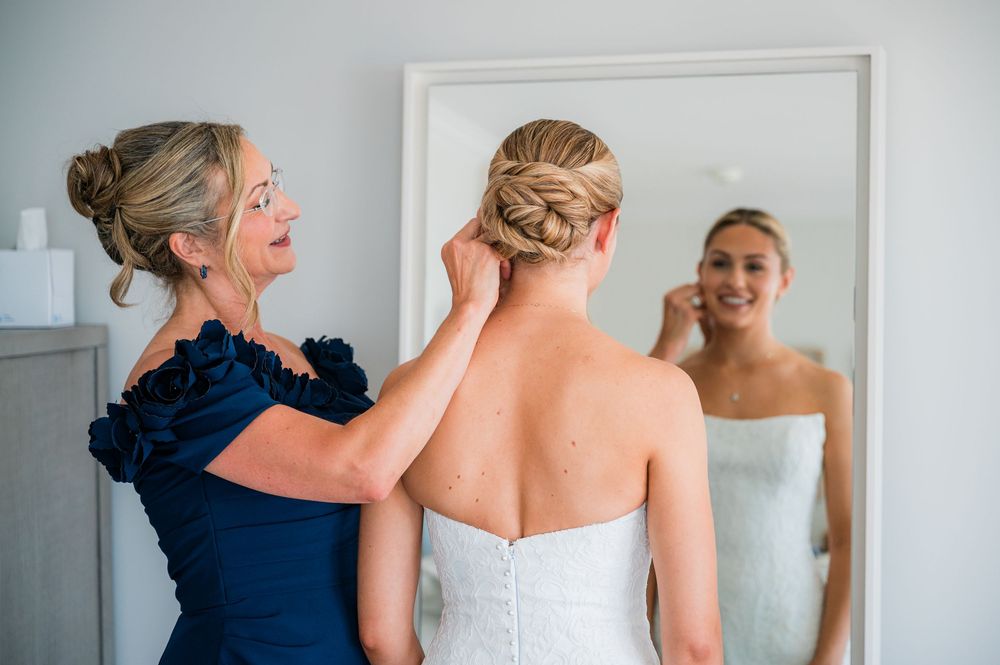 A bride in a strapless wedding gown gets help with her dress from someone wearing navy blue.