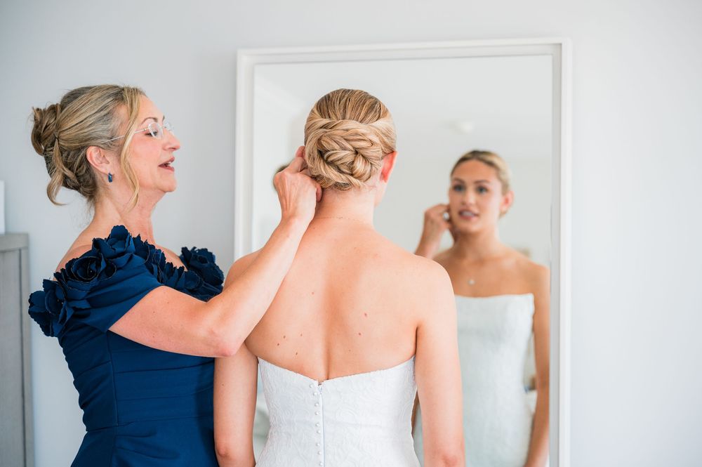 A bride in white and bridesmaid in navy share a candid moment while getting ready for a wedding ceremony.