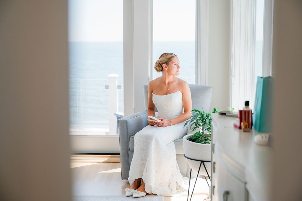 A bride in a white strapless gown holds a pastel bouquet in a bright sunlit room.