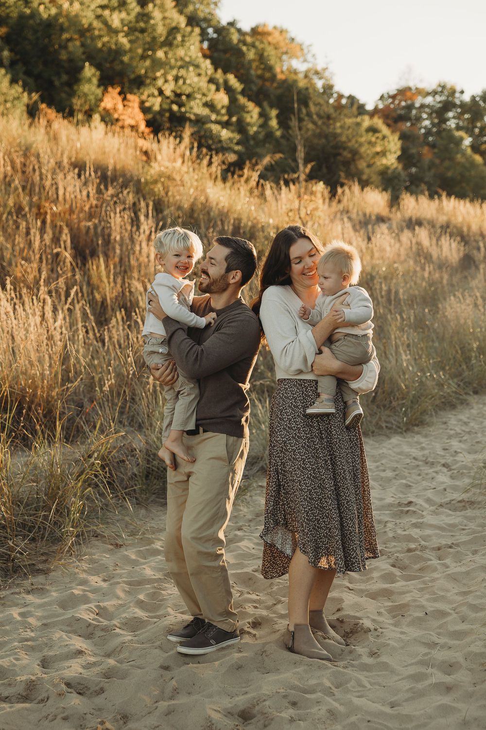 A group stands together on a sandy beach path during golden hour as warm sunlight filters through tall grass.