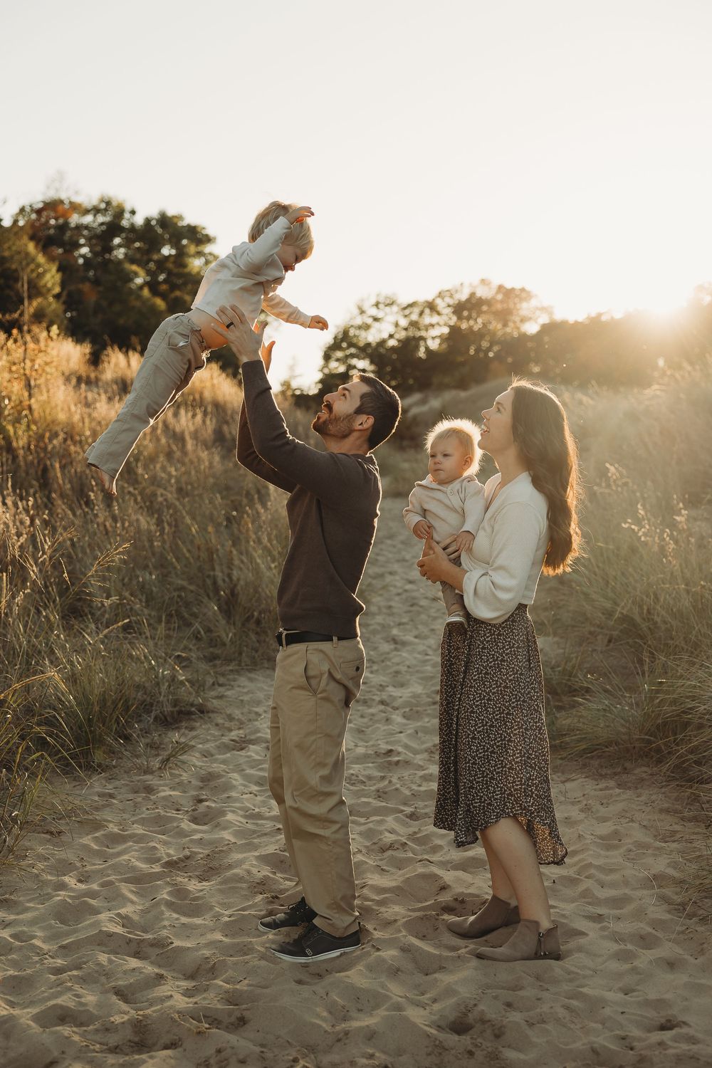 A couple dances joyfully together on a sandy beach path at sunset, creating romantic silhouettes against the golden light.