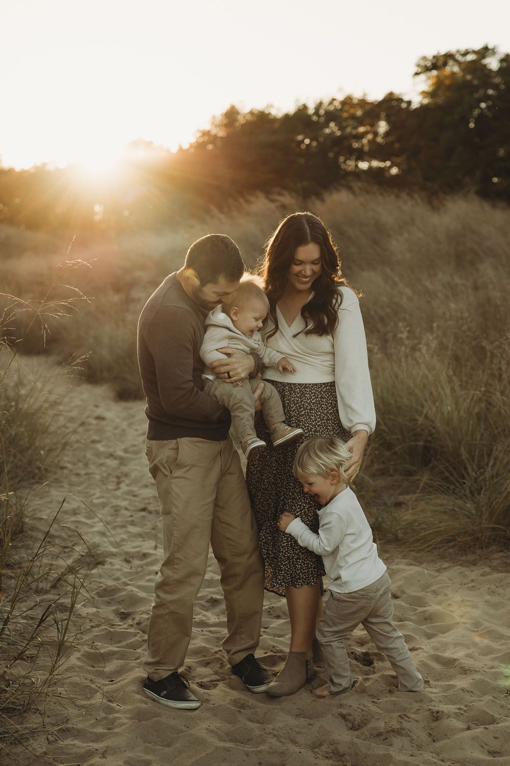 A family shares tender moments together on a sandy beach during golden hour sunset.