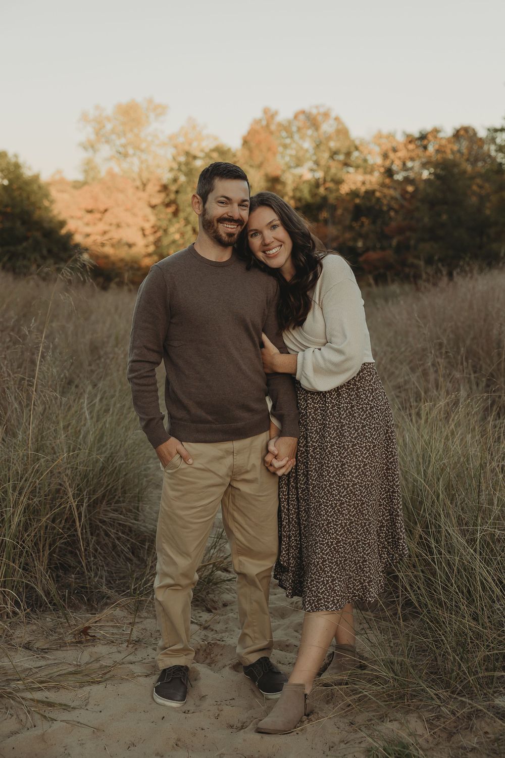 A couple shares an intimate moment while posing together in tall grass during sunset.