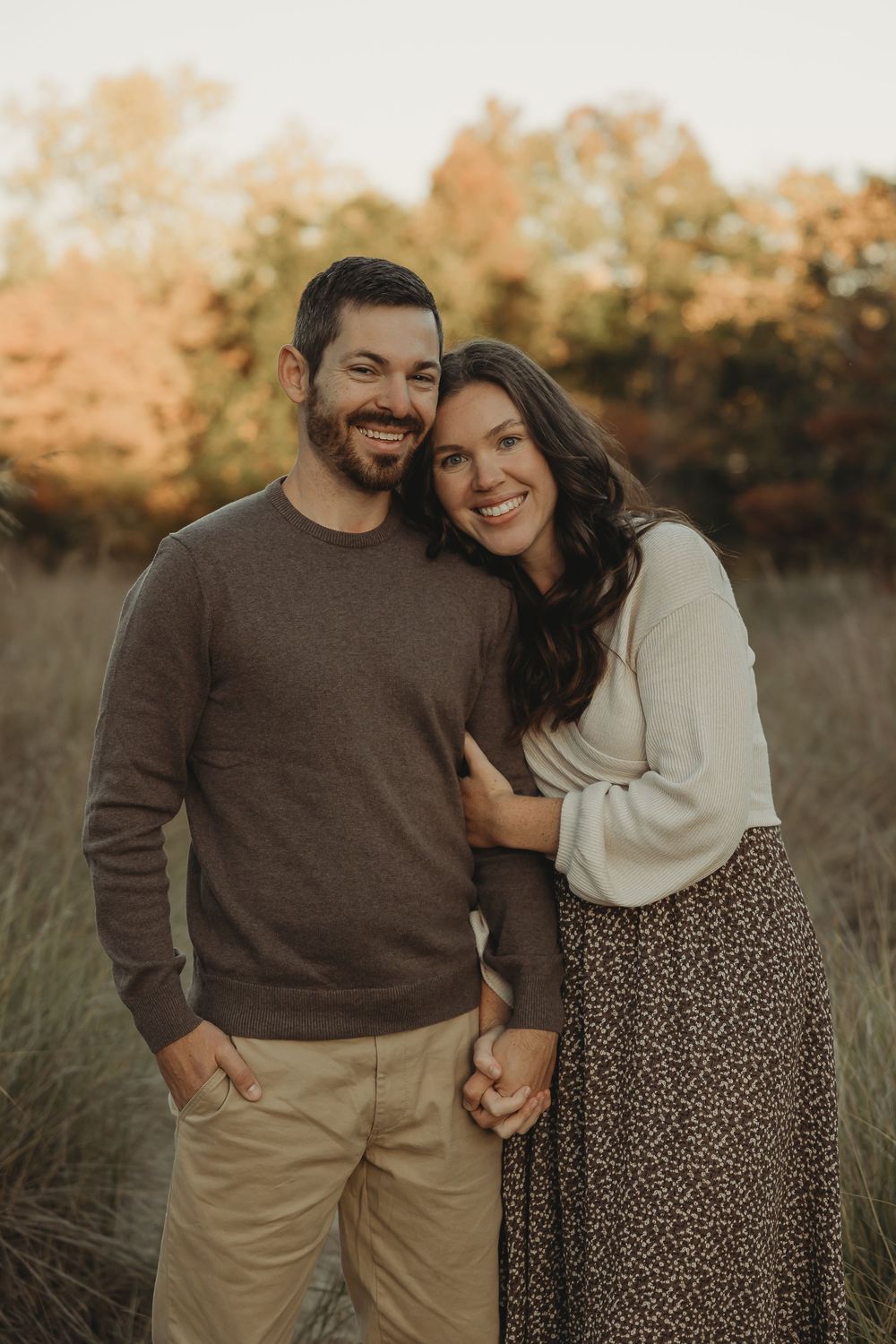 A couple shares a tender moment in a field during golden hour wearing coordinated fall outfits.