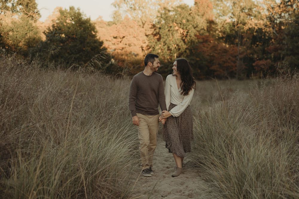 A couple stands together in a golden field during sunset while holding hands and sharing an intimate moment.