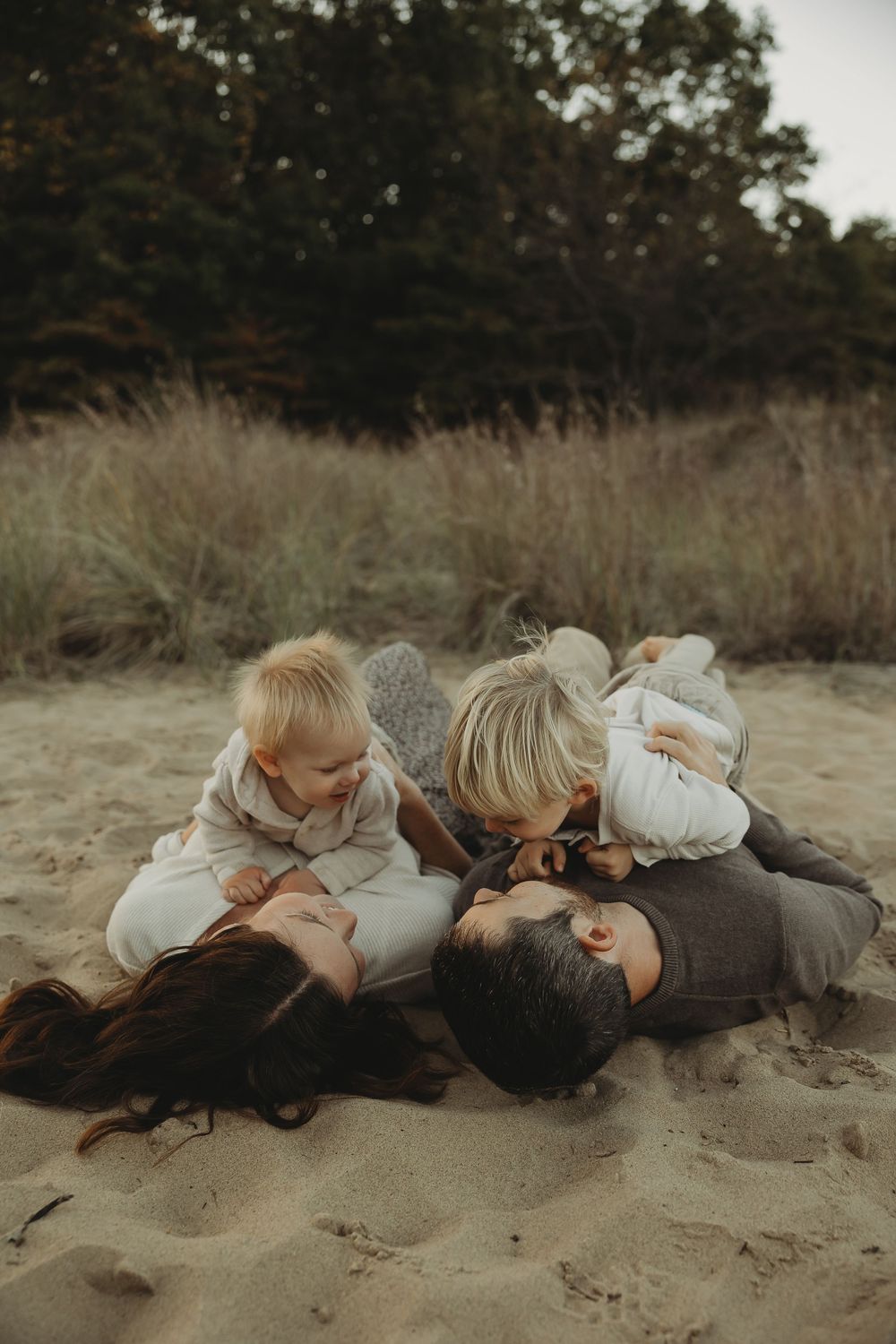 Two people lying close together on sandy beach at sunset wearing light colored clothing.