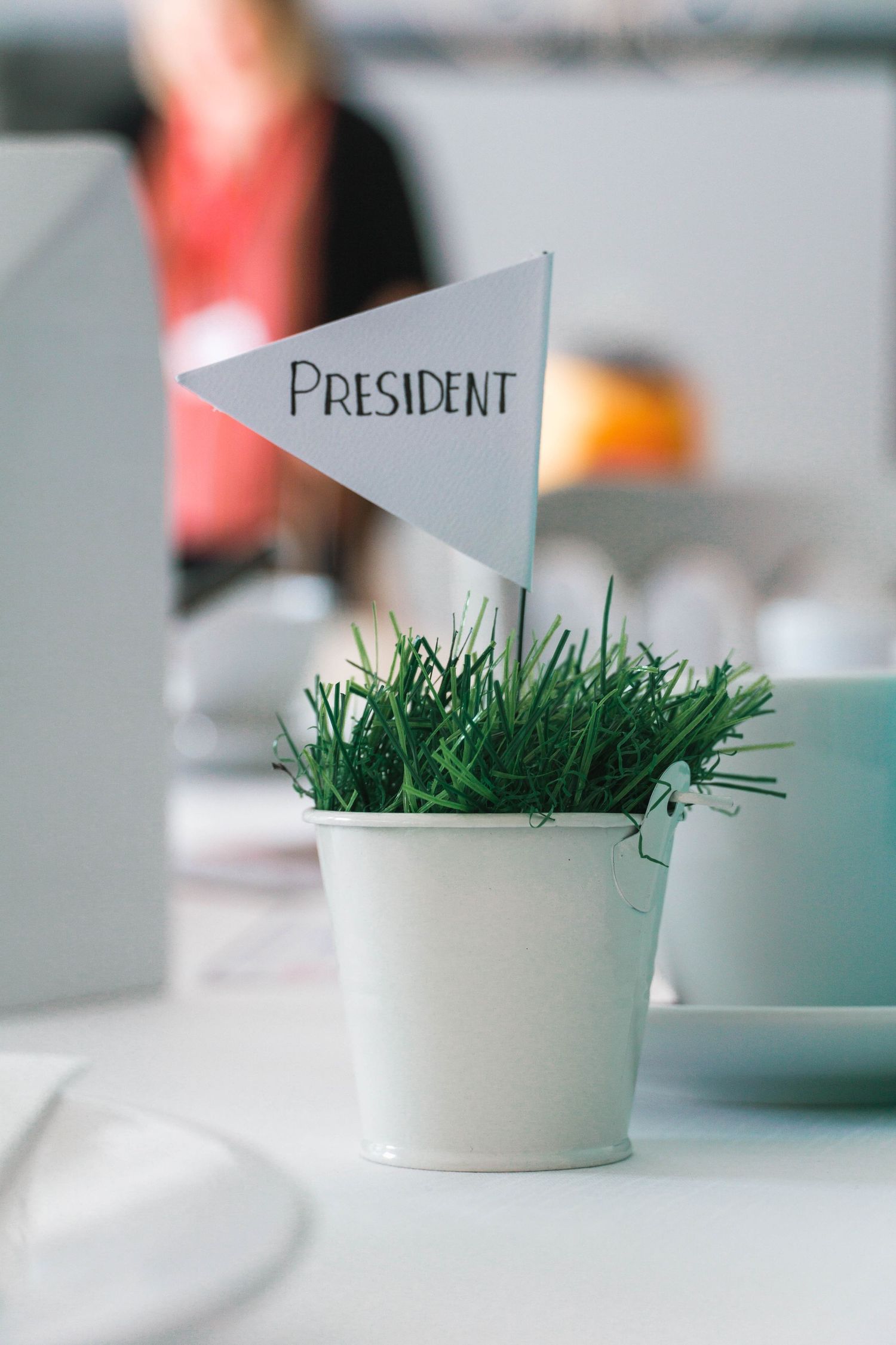 White bucket with green grass and white flag that says president. Place marker at an event.
