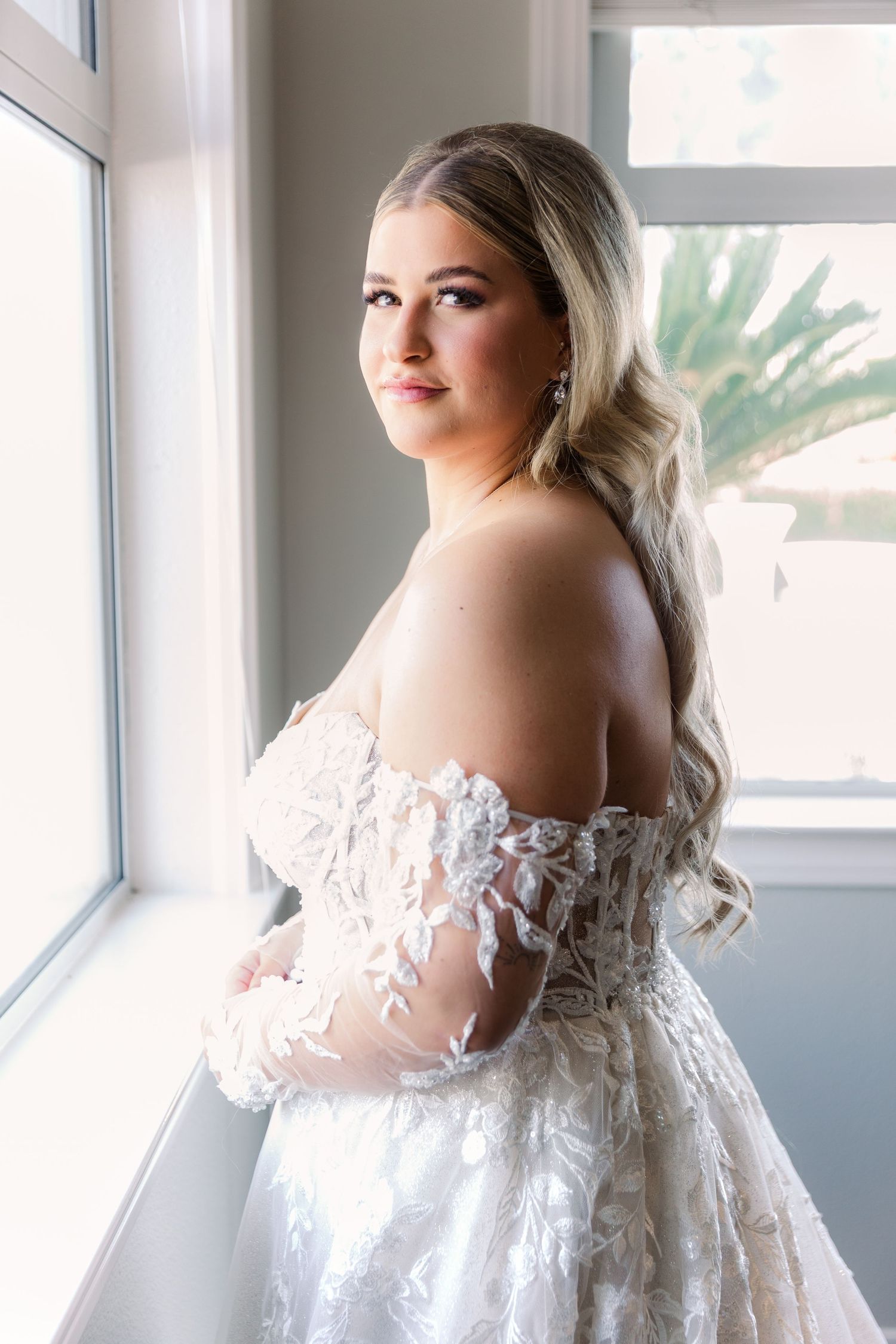 Elegant bridal portrait by a window showcasing intricate lace details of a wedding gown.