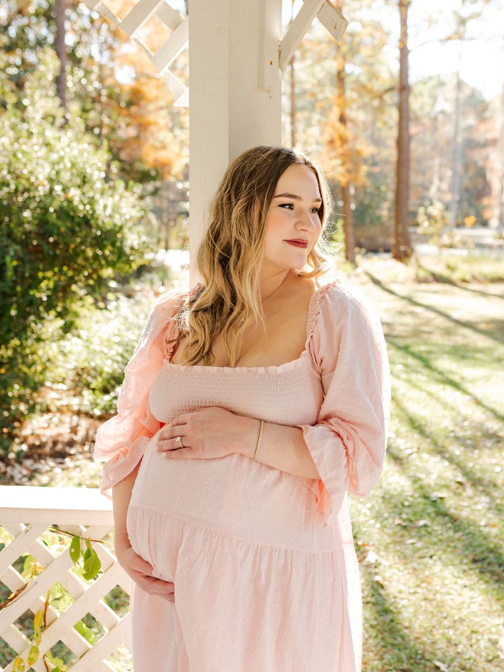 A flowing pink dress captures the sunlight in a garden gazebo setting.