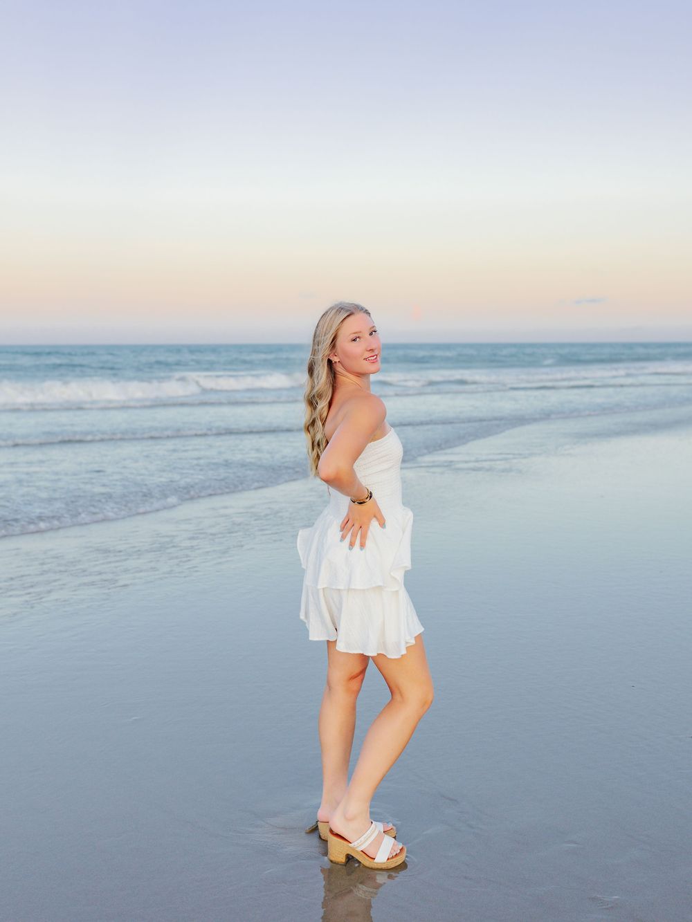 A dreamy beach sunset photo with someone in white clothing walking along the shoreline.