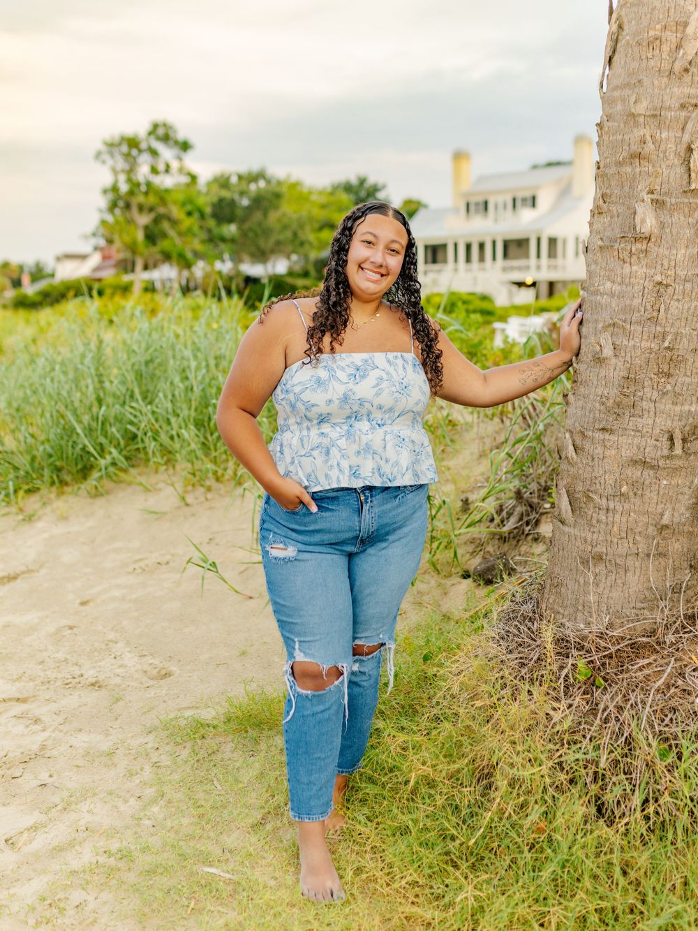 Person in blue top and ripped jeans poses casually by palm trees on beach trail.