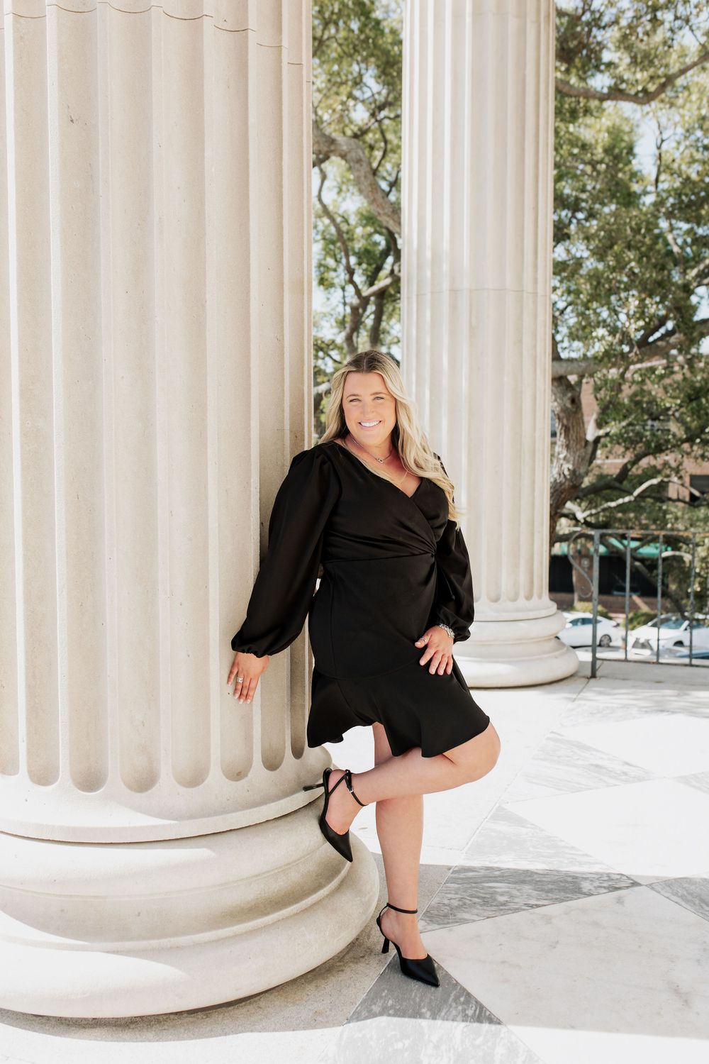 Fashion photo featuring a black wrap dress and heels posed by white classical columns.