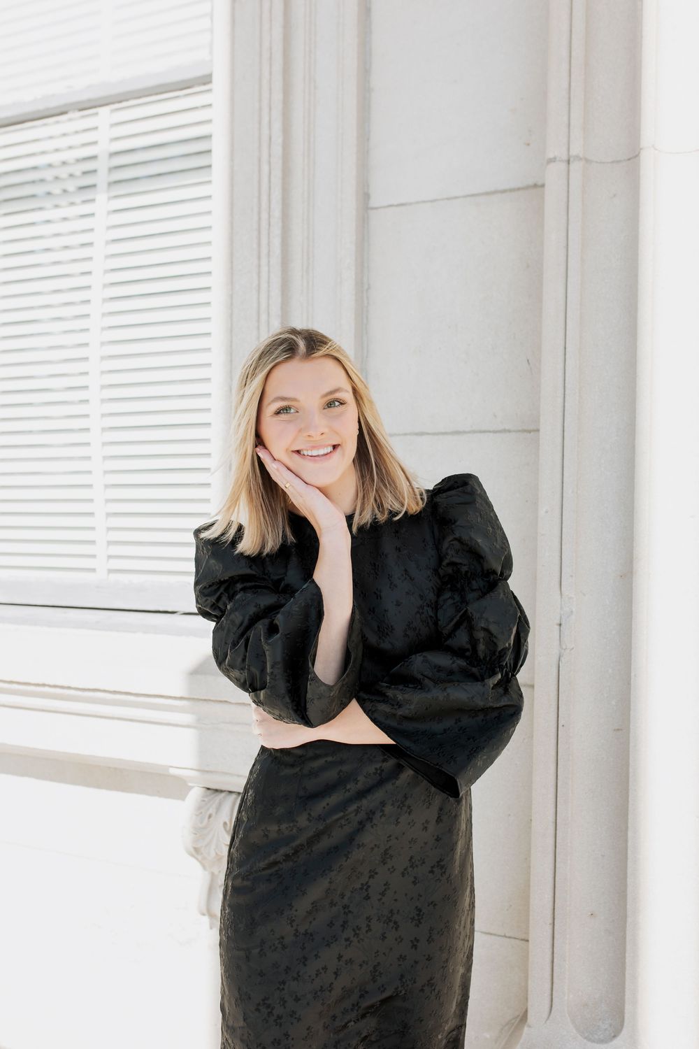 Black textured dress with statement sleeves photographed against a white architectural backdrop.