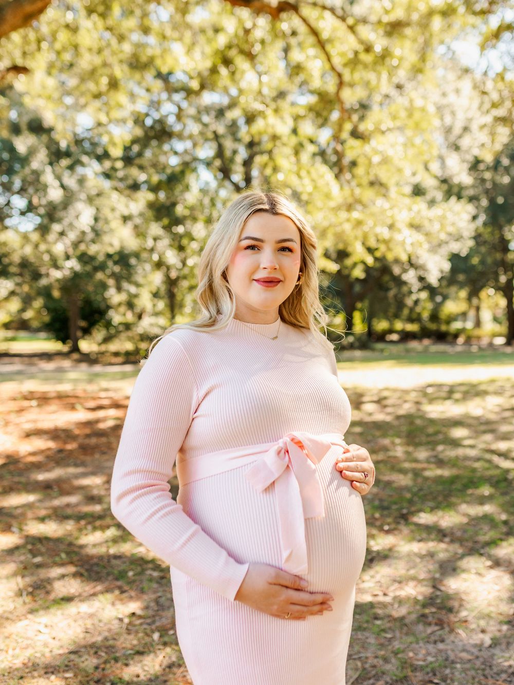 Outdoor maternity photo with golden sunlight filtering through trees.