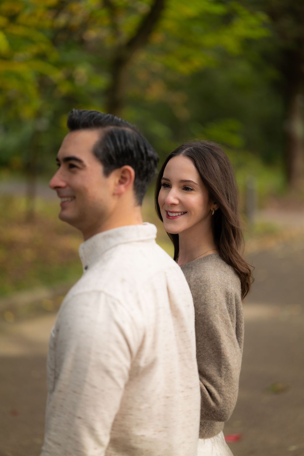 Woman smiling over her shoulder at man while walking together on a tree-lined autumn park path.