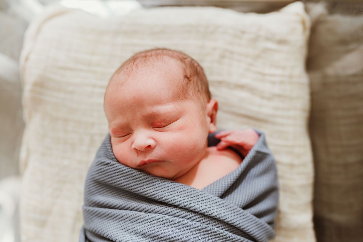 A sleeping newborn baby wearing a gray striped onesie rests peacefully on white bedding.
