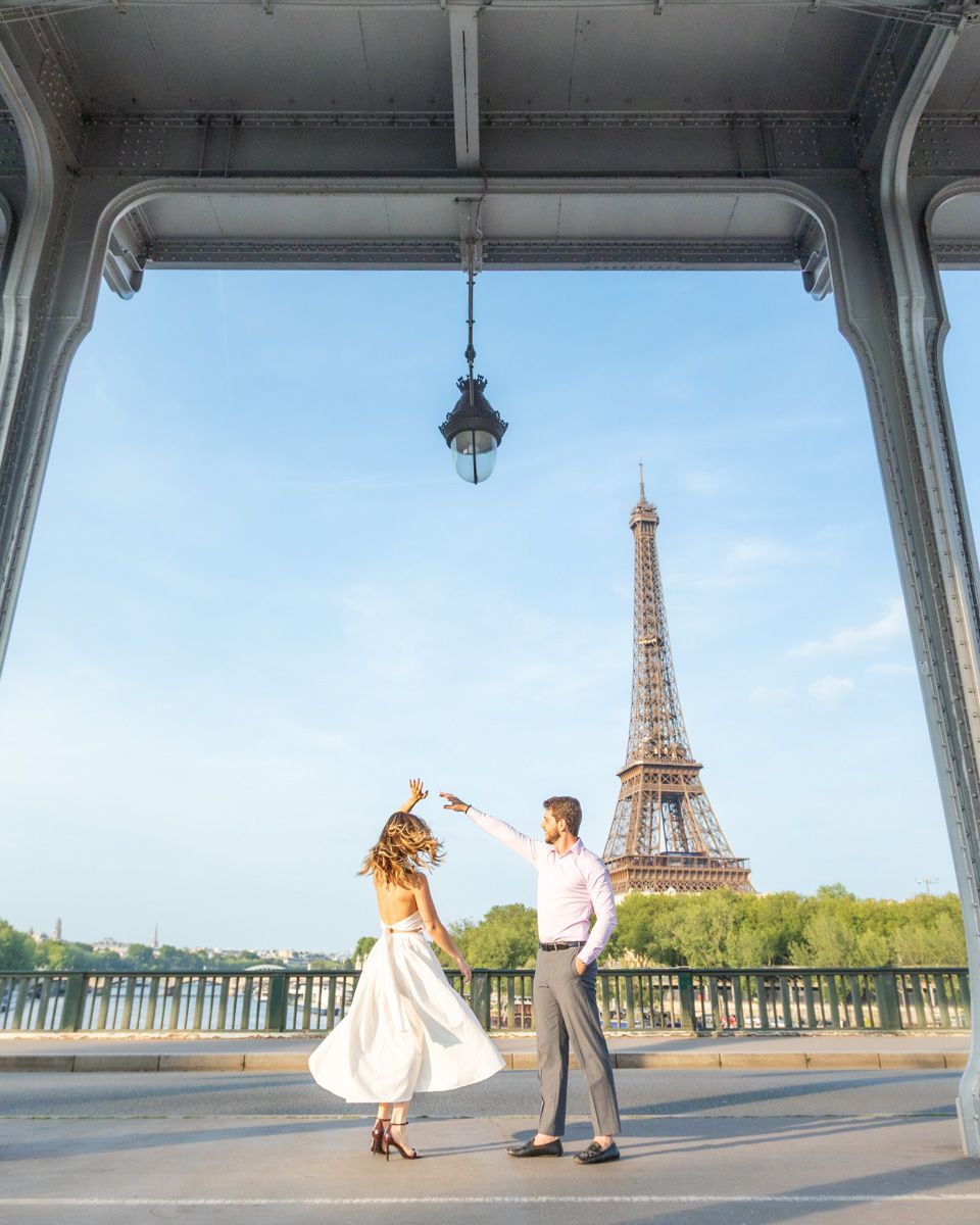 Couple dancing elegantly in front of the Eiffel Tower in Paris during a bright sunny day.