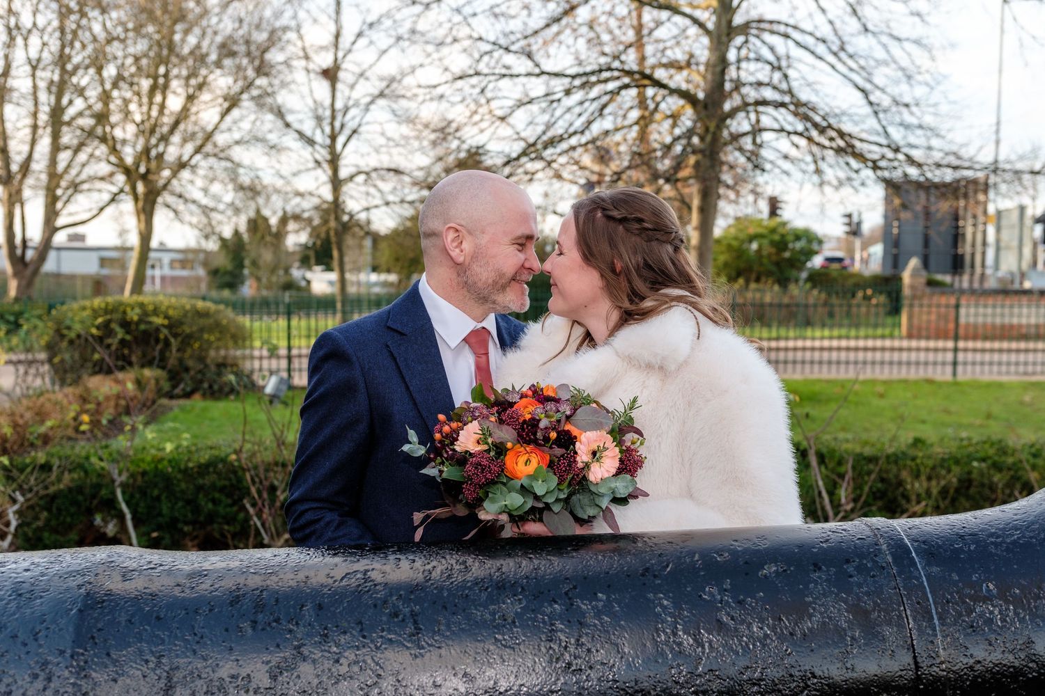 A wedding couple shares an intimate moment on a stone wall with autumn flowers and greenery in the background.
