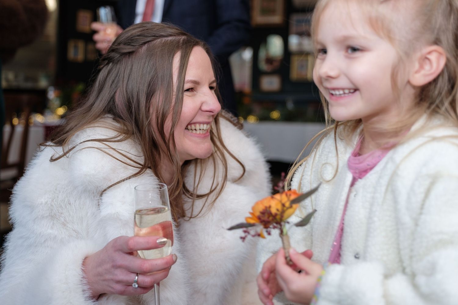 A woman in a white fur wrap shares a lighthearted moment with a young girl at a celebration.