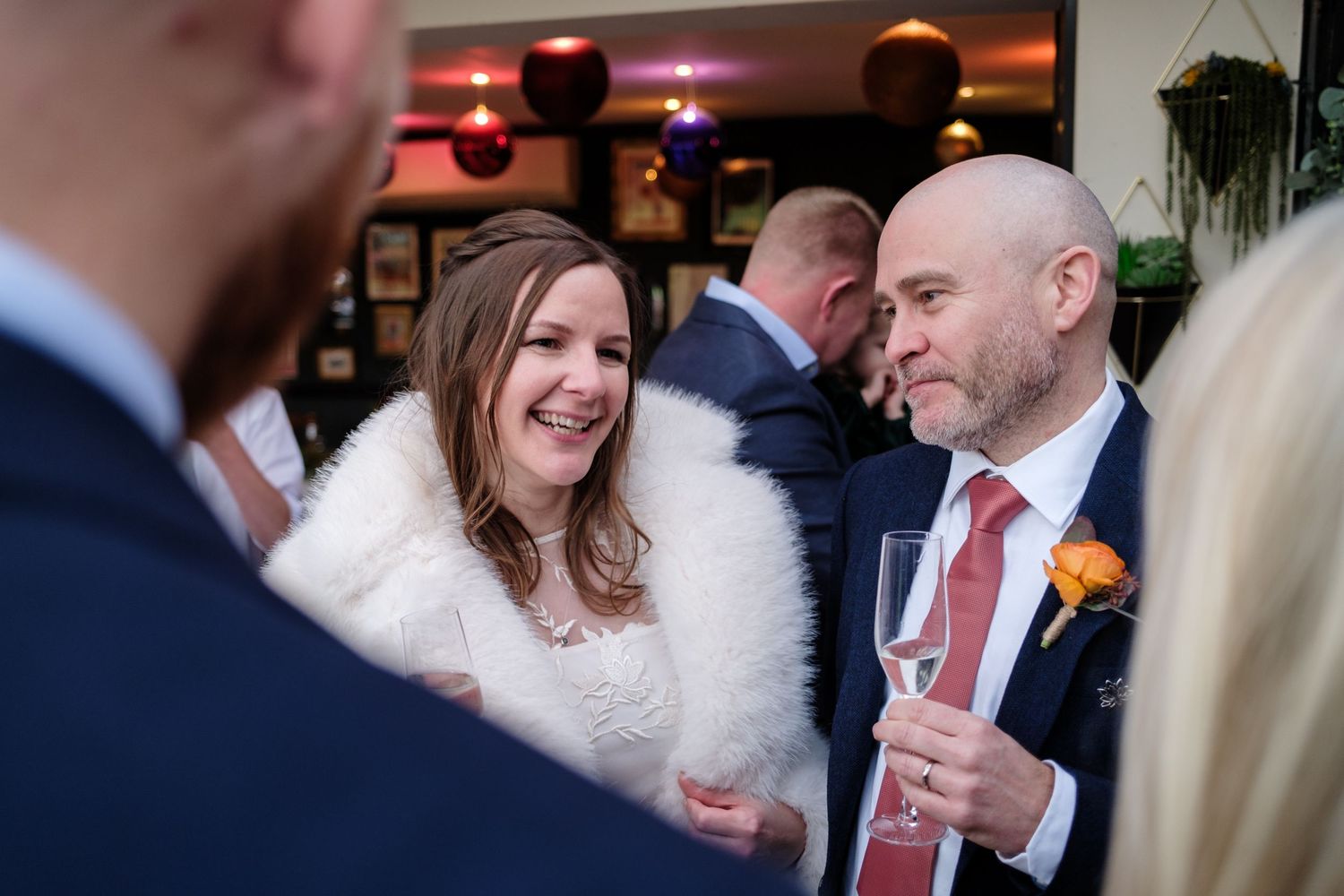Wedding guests in winter attire share a joyful moment during an indoor reception celebration.