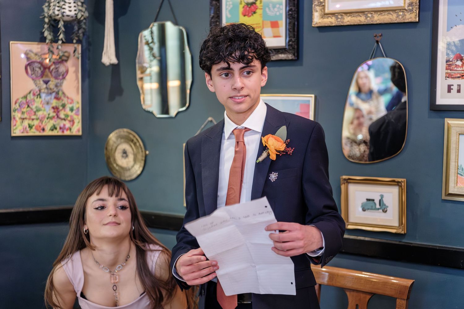 A couple celebrates during their wedding ceremony in a cozy room with teal walls decorated with framed artwork.
