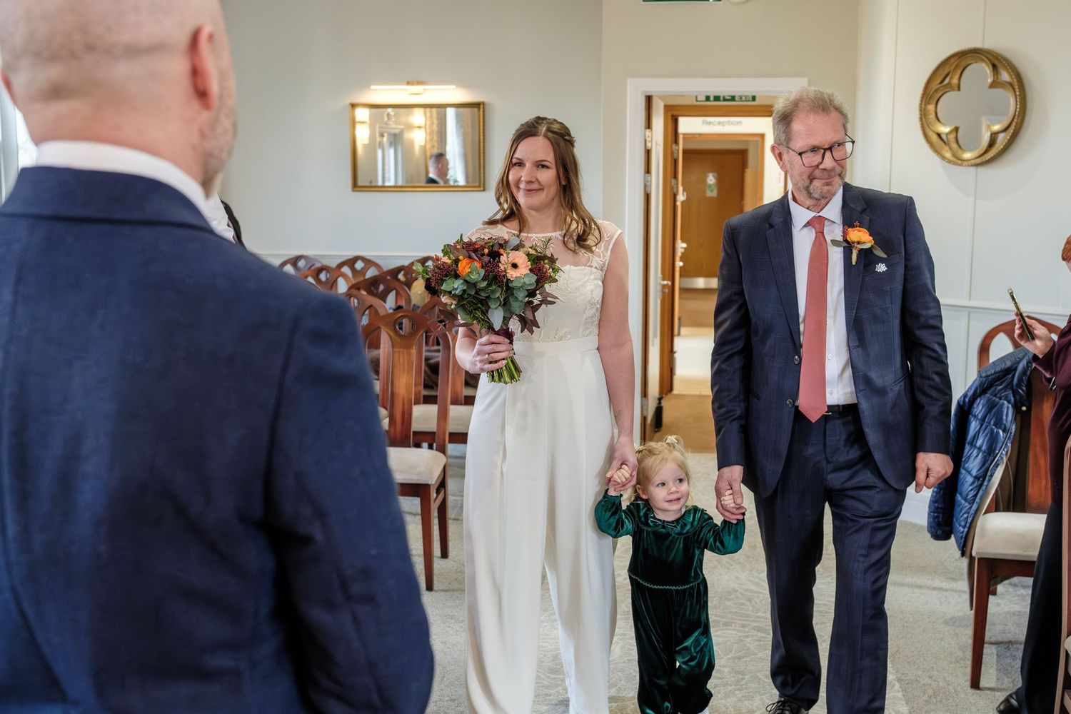 A wedding ceremony moment in a bright interior room with white decor and floral arrangements.