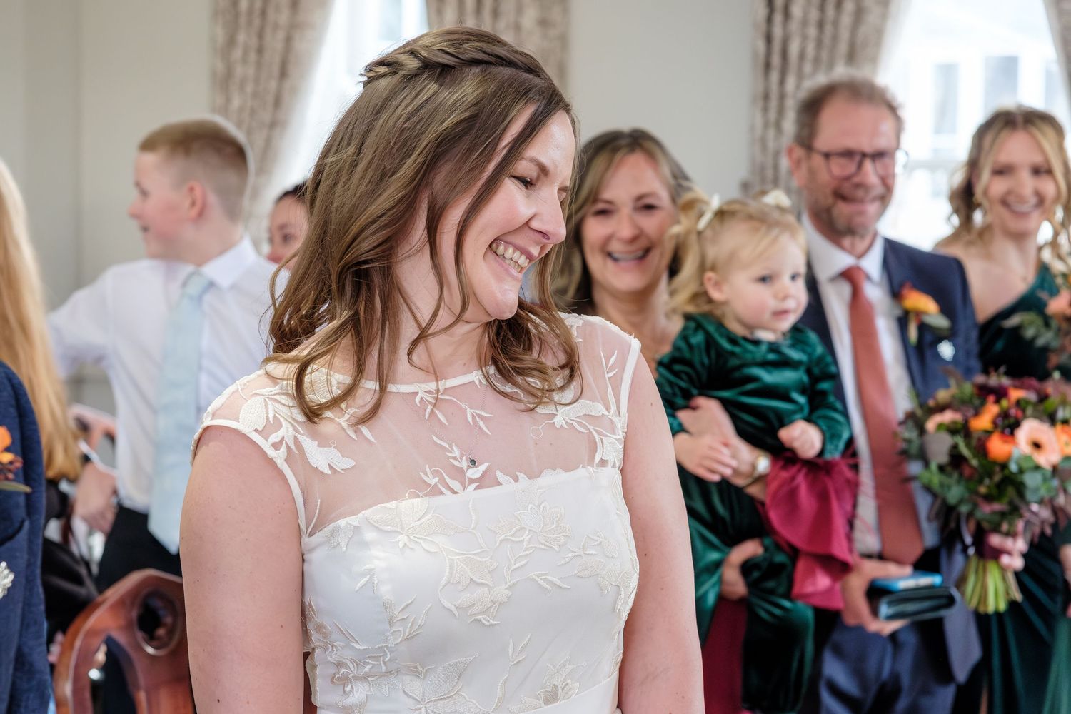 A joyful wedding celebration with a bride in a white lace dress while guests smile in the background.