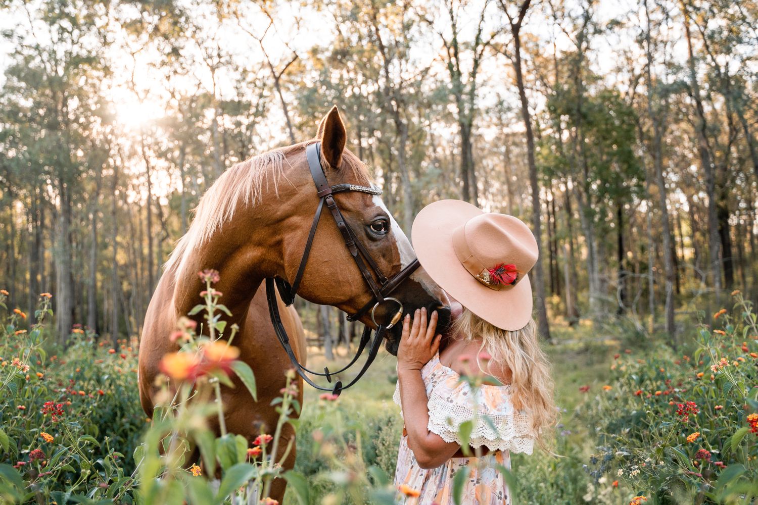 A horse and someone in a pink hat share a tender moment in a sunlit forest with wildflowers during a portrait photoshoot with a horse Sydney