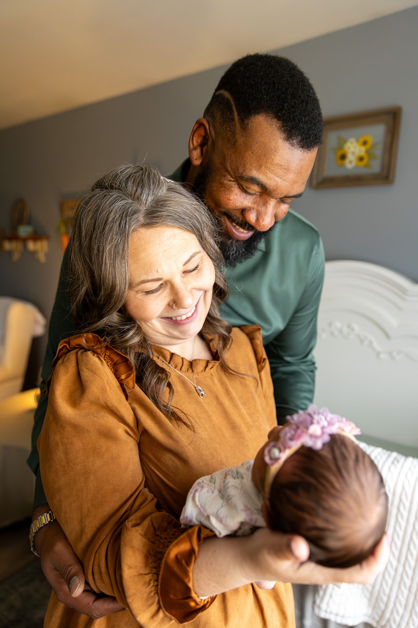 Grandparent and father laughing joyfully while holding newborn baby girl.