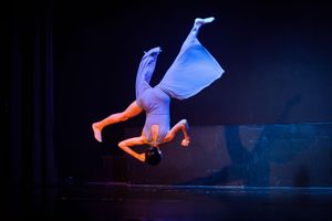 Modern dance performance with dramatic lighting and flowing movements on a dark stage.
