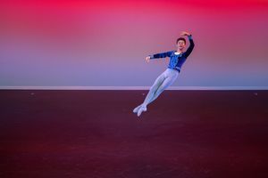 Dancer performing a dramatic leap against a red-tinted backdrop.