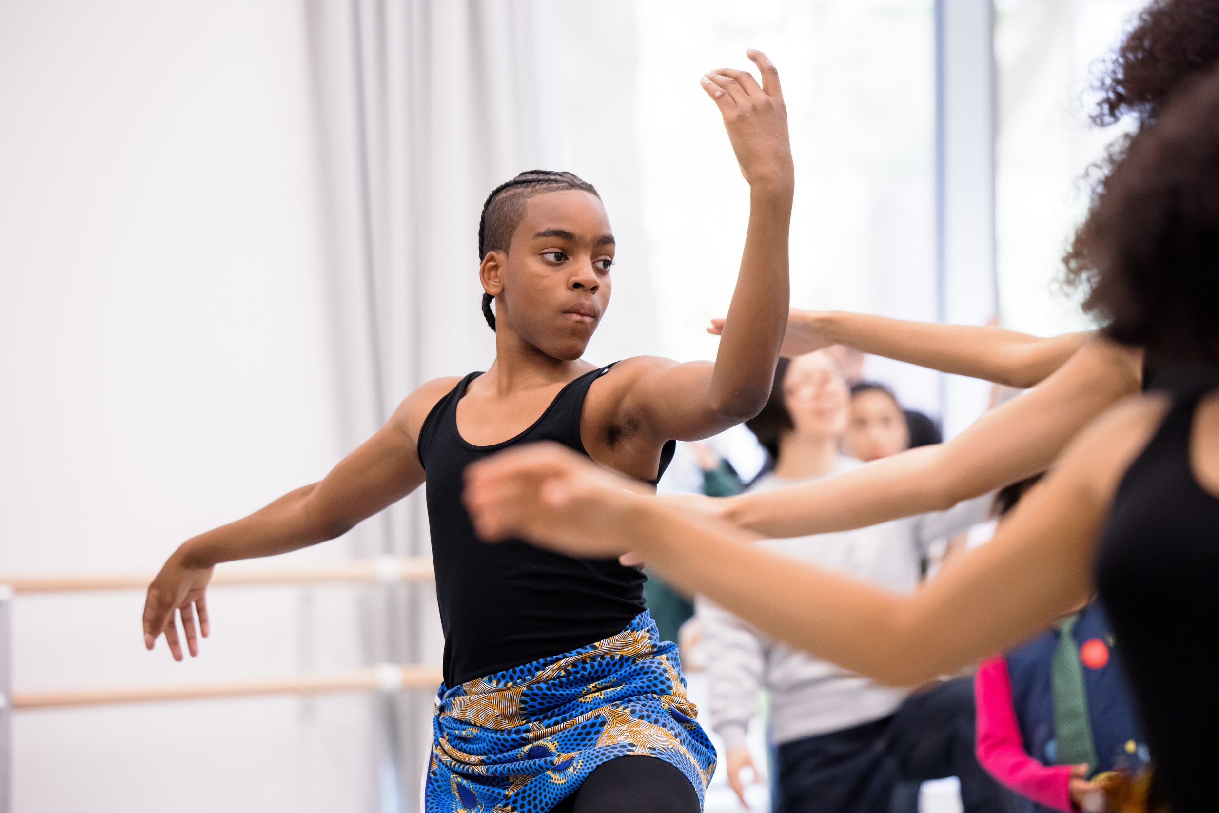 Dance class participants moving energetically in a bright studio with mirrors.