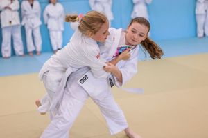 Children practicing martial arts moves in a bright dojo with blue mats and white uniforms.
