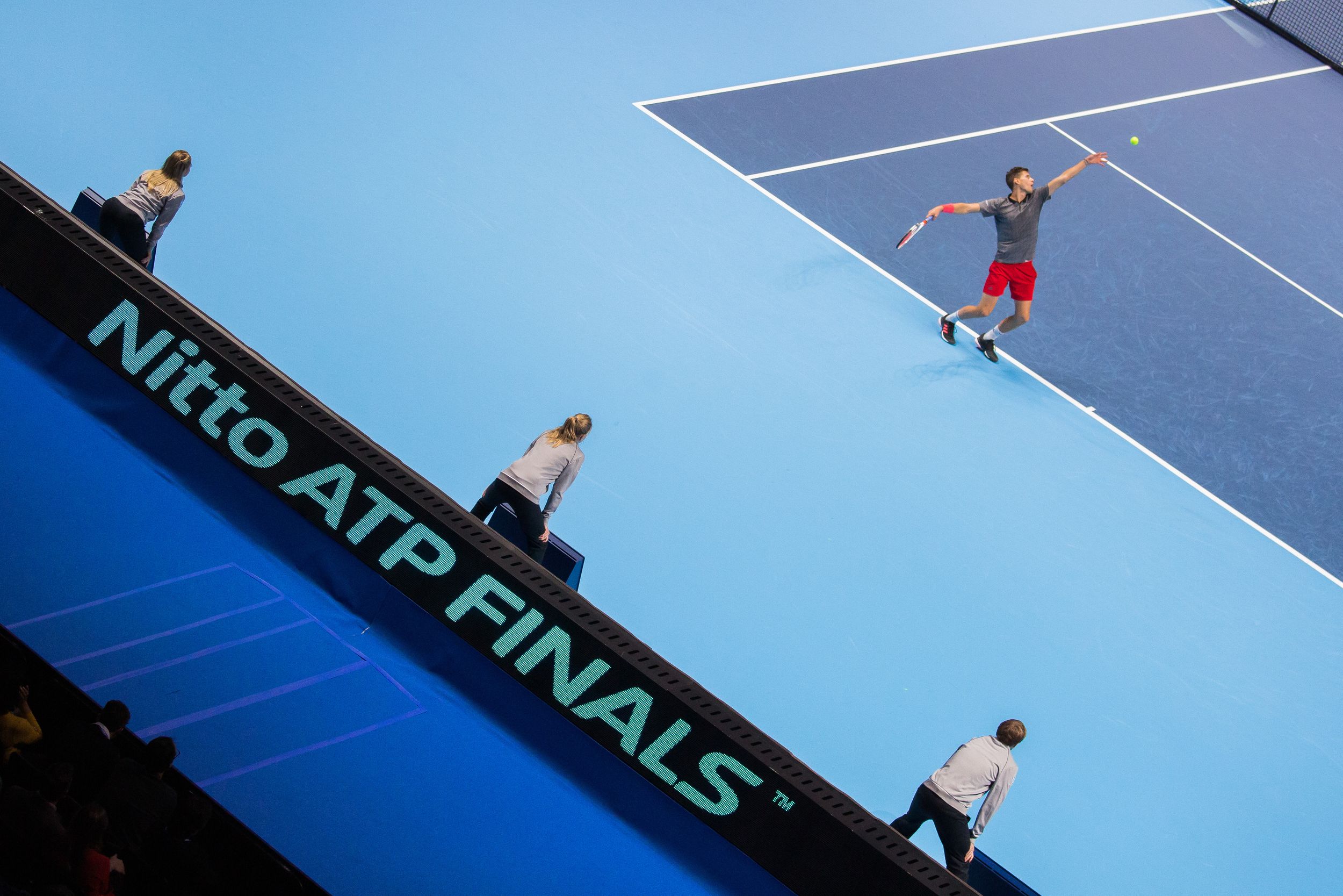 Professional tennis player serving on a bright blue hardcourt during a tournament match.