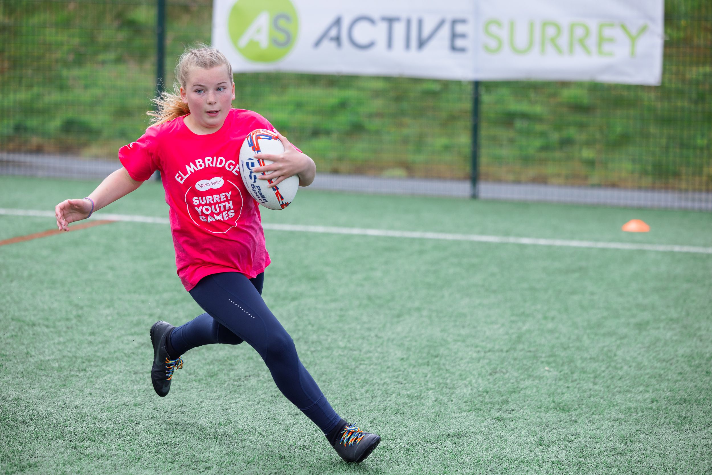 Children playing sports on an outdoor artificial turf field with Active Surrey banner visible.