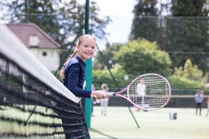 Young players practicing tennis outdoors on a sunny day with rackets.