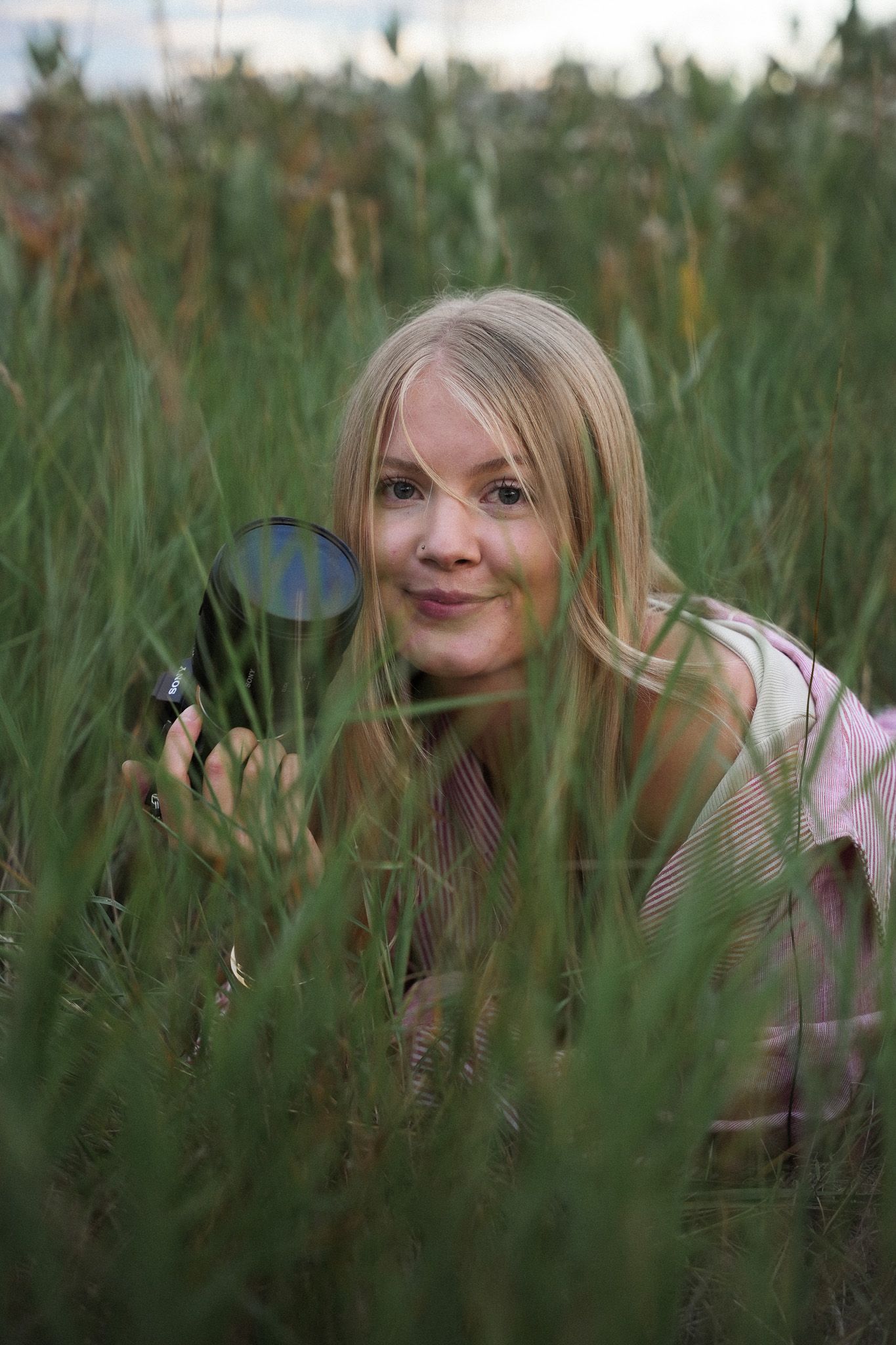 A person playfully peeks through tall grass in a natural outdoor setting during golden hour.