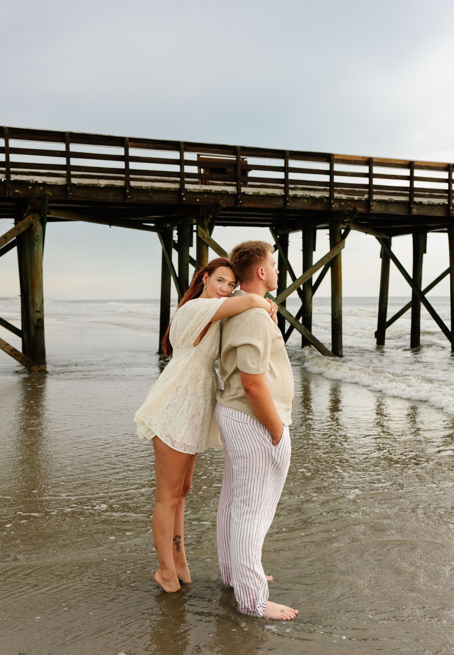 Romantic autumn engagement photo session showing couple embracing against large tree trunks in a wooded setting.