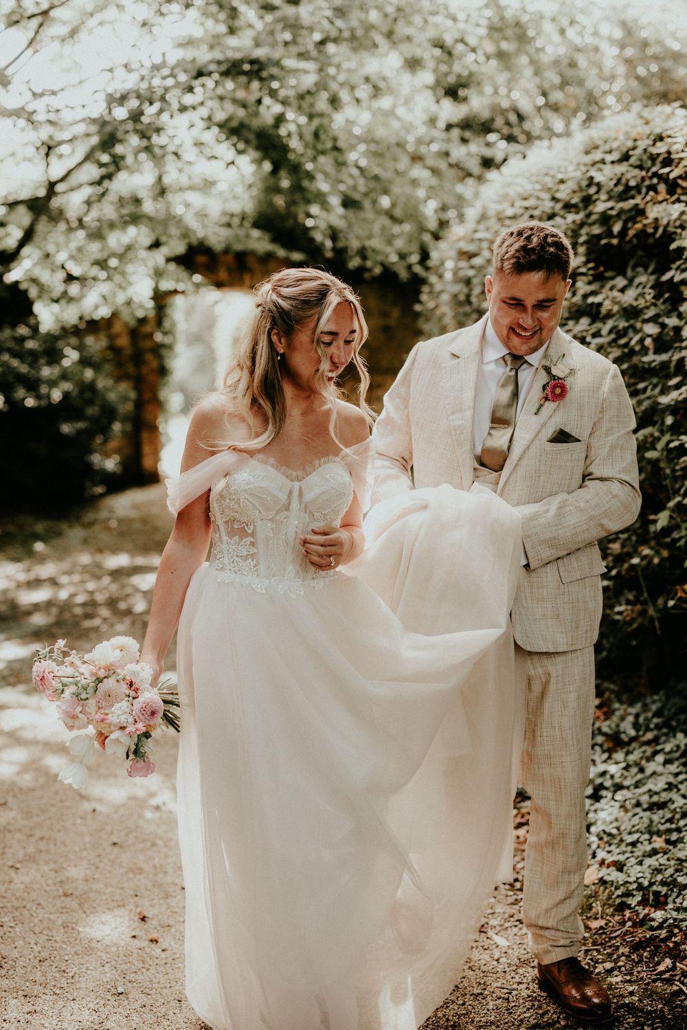 A couple shares a joyful moment on their wedding day in a garden setting, wearing white and beige attire.