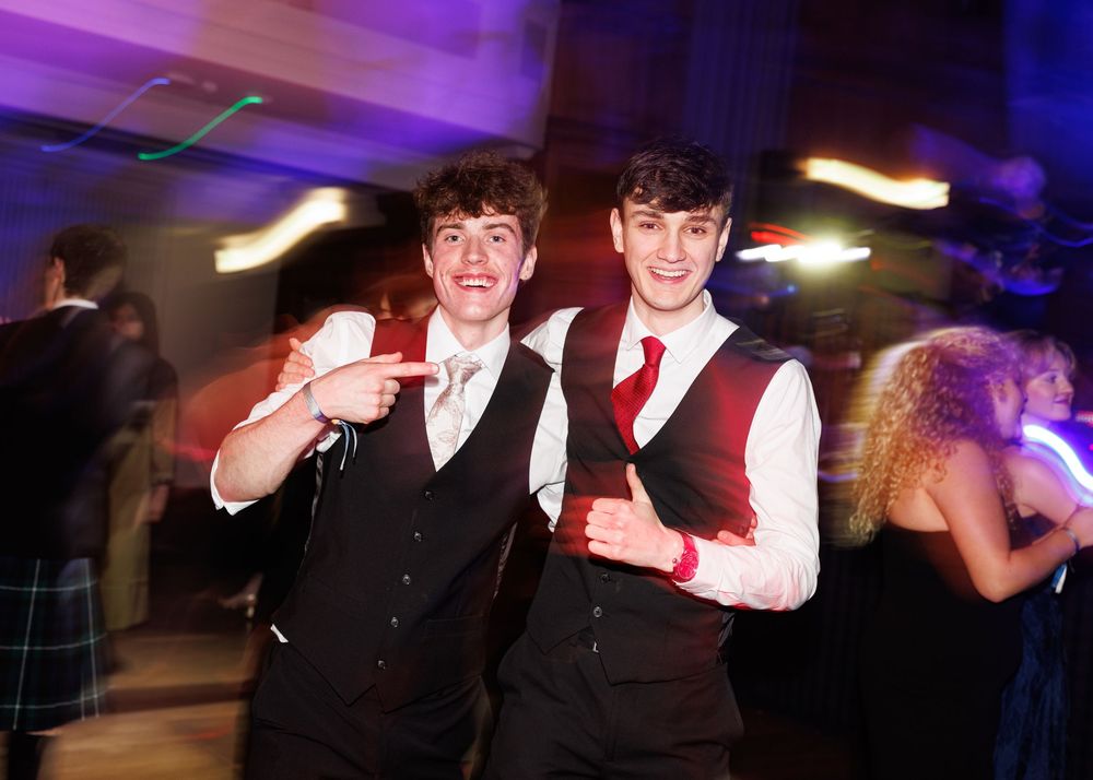 People dancing and celebrating at a party with purple and blue lighting effects in the background.