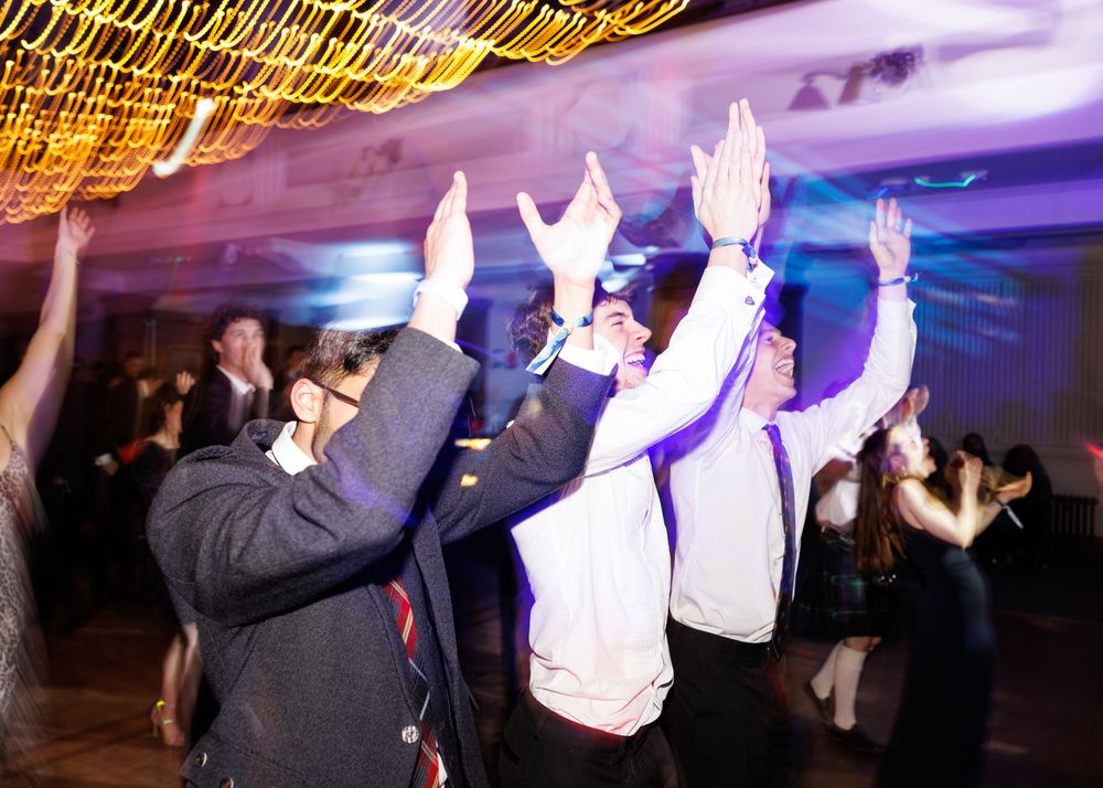 Party guests dancing with hands raised under golden string lights at a nighttime celebration event.