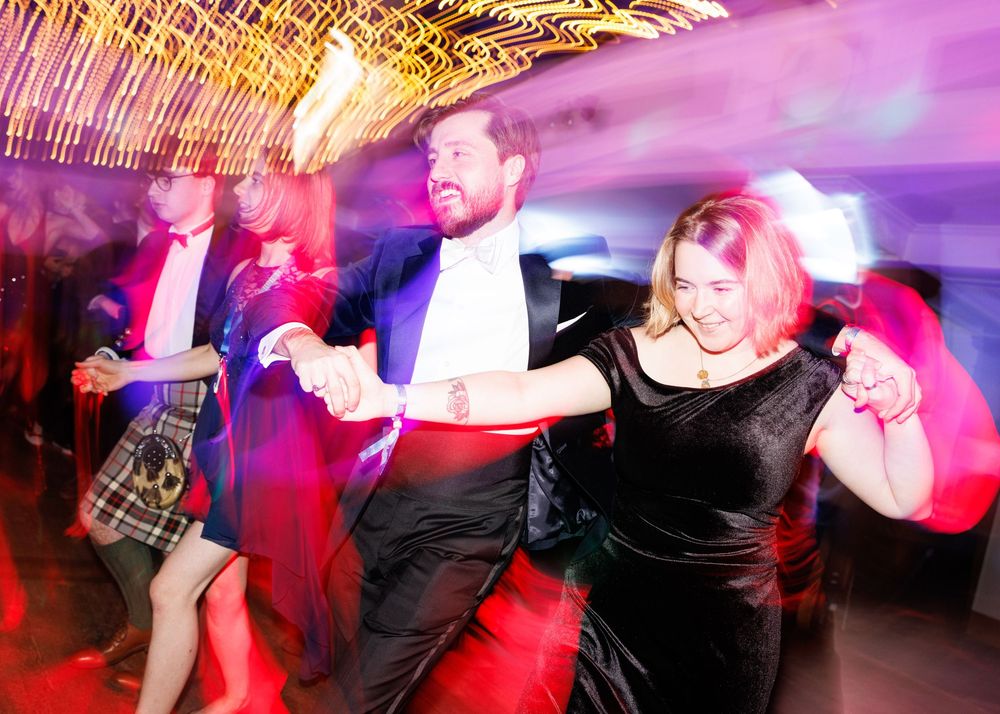 Dancers moving energetically on a nightclub dance floor illuminated by colorful pink and red lighting.
