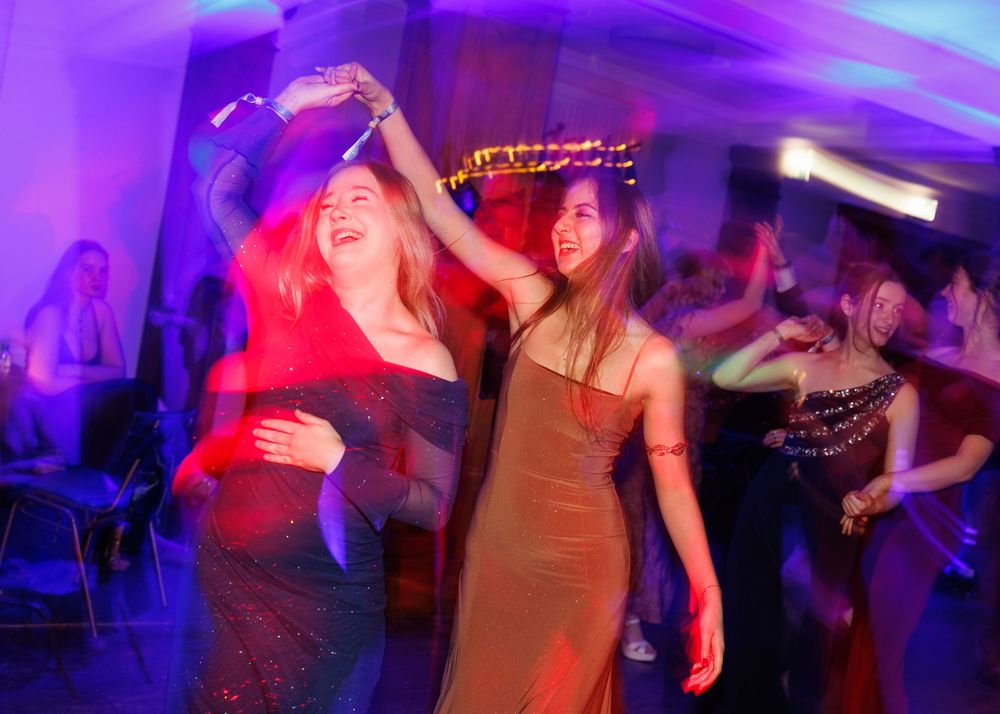 People dancing and celebrating at a nightclub with colorful purple and red lighting effects.