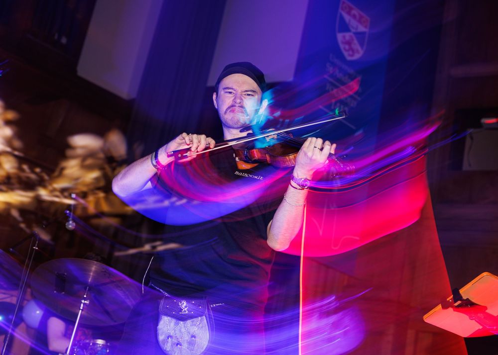 DJ performs on stage with turntables under vibrant red and blue lighting at a nightclub event.