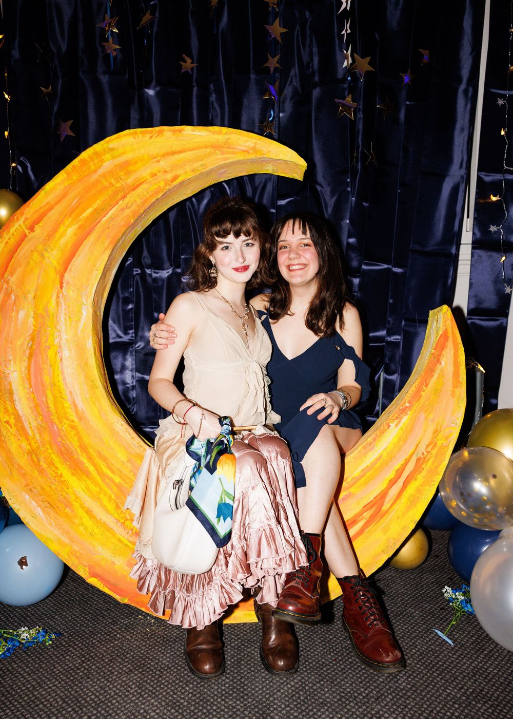 A creative photo series showing people posing with a large decorative yellow crescent moon prop against a dark backdrop.